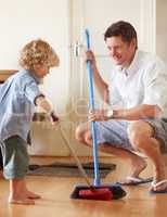 Keeping things clean. A father and toddler son sweeping up sand together in their home.