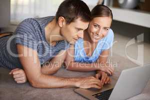 Getting all their info online. Shot of a happy young couple using a laptop on the floor together.