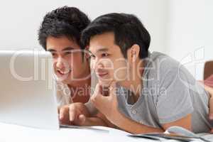 Finding everything theyre looking for.... Two young Asian guys searching the internet together on a laptop.