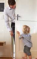 Playing peekaboo. A little boy playfully push a door closed while his father stands on the other side.