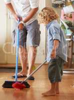 Keeping things clean. A father and toddler son sweeping up sand together in their home.