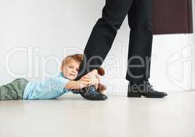 Separation anxiety in action. Portrait of a cute young boy holding onto his dads leg as he tries to leave for work.