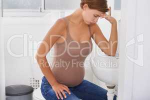 Riding waves of nausea. A pregnant woman struggling with morning sickness in the bathroom.