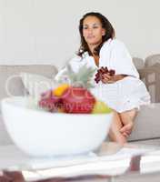 Cute woman at home eating fruits. Young woman in a bath robe having fruits at home.