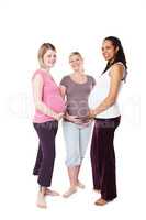 Already feeling protective. Three pregnant women smiling broadly at the camera while standing against a white background holding their stomachs.