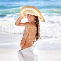 Gorgeous young beauty. A beautiful young woman posing in a woven sunhat and sarong at the beach.