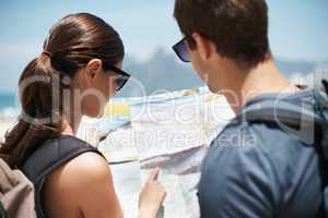 Plotting the best route to the beach. Shot of a young couple looking at a map while standing on a beach.