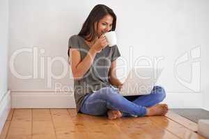 Wireless connectivit. Shot of a young woman sitting on the floor at home drinking a coffee and using a laptop.