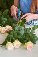 Shes learned the skills necessary for great arranging. High angle shot of a florists hands trimming leaves off of rose stems.