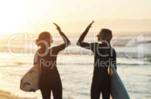 High fives and high tides. Rearview shot of a young couple joining hands for a high five while surfing at the beach.