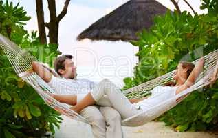 Relaxation and romance - VacationsGetaways. Shot of a happy couple relaxing on a hammock together in their own private paradise - Romance.