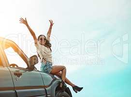 Enjoying life as one whirlwind of an adventure. Portrait of a young woman sitting on a car with her arms outstretched while on a roadtrip.