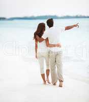 A romantic, scenic stroll. Rear-view of an affectionate young couple pointing to the ocean while on a romantic stroll.