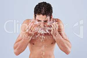Purely refreshing. Studio shot of a bare-chested young man splashing water on his face.