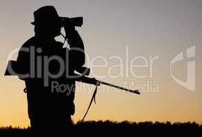 Tracking wildlife. A silhouette of a game ranger holding his rifle and looking through his binoculars at sun rise in the outdoors.