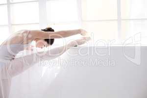 Grace in movement. Supple young ballerina stretching alongside a white wall.