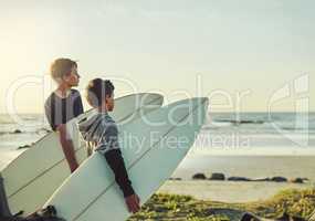 The waves are waiting. Shot of two young brothers holding their surfboards while looking towards the ocean.