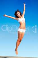 Im feeling @ing fantastic. An energetic young woman jumping while against a blue sky.