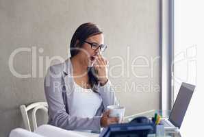 Some days seem longer than others. An attractive young businesswoman yawning while sitting at her desk.