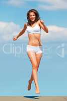 Happily living on the edge. Action shot of a woman running on a buildings roof against a blue sky.