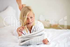 This article is very interesting. Young woman lying on the bed at home and reading the newspaper.