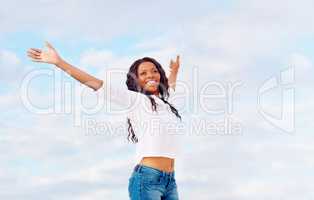 Living to the fullest. Happy young woman standing against a blue sky with her arms outstretched.