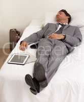 Work exhaustion. A handsome young businessman sleeping on the bed with his digital tablet.