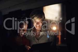 What is our next big move. Shot of two businesswomen using a digital tablet together in an office at night.