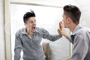 Suppressed emotions. Young man looking at a screaming reflection of himself in a mirror.