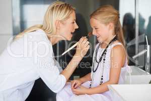 They share a playful bond. Little girl having make-up applied by her mother with a smile.