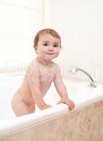 Bath time is over. An adorable baby girl climbing out of the bath.