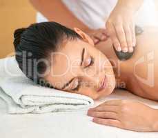 Indulging in a much needed massage. Cropped shot of an attractive young woman enjoying a hot stone massage at a spa.