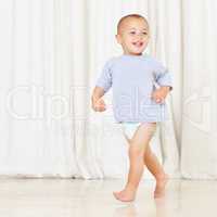 Strutting his stuff. Full length shot of a cute little boy walking around the house in a nappy and t-shirt.