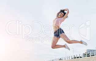 Get out and get loose. Shot of a young woman jumping into mid air at the beach.