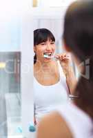 Keeping those pearls white. Shot of a cheerful attractive young woman brushing her teeth while looking at her reflection in a mirror at home during the day.