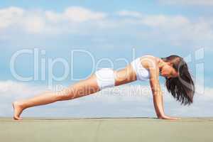 Shes disciplined as can be. Side view of a young woman doing push-ups on a roof against a blue sky.