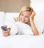 Movies in bed. An attractive young woman switching channels with the tv remote.