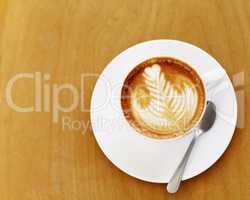 Made by an skilled barista. High angle shot of an artistically prepared cup of cappuccino sitting on a cafe table.