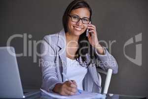 Giving helpful advice to her clients. An attractive young businesswoman talking on the phone while working at her desk.