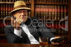 He heads up a large criminal organisation. Aged mob boss wearing a hat and looking serious while pointing.