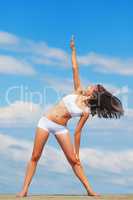 Stretching beauty. A young woman doing yoga on a roof against a blue sky.