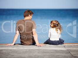 Sharing her dreams with daddy. Rear-view of a young father and his daughter sitting on a pier with the ocean in the background.