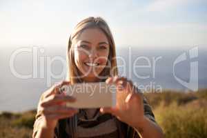 A moment worth remembering. Portrait of an attractive young woman holding up her cellphone to take a photo outdoors.
