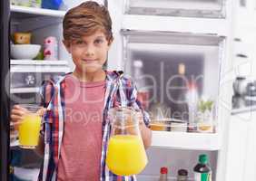 Some goodness to quench the thirst. Shot of a young boy standing in front of the fridge with some orange juice.