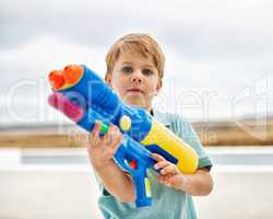 Im a professional water shooter. Portrait of a cute young boy holding a water gun outside.