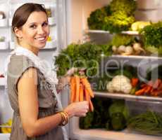 Shes stocked up on healthy food. Smiling woman adding some fresh carrots to her fridge already stocked with raw vegetables.