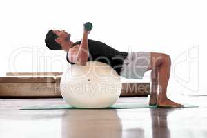 He found a way to make lying down a workout. Full length shot of a man lifting weights while lying on an exercise ball.
