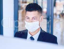 First rule of office work Wear a face mask. Shot of a young businessman wearing a face mask and using a computer in a modern office.