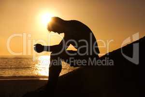 Contemplating the meaning of life. Silhouette of a man sitting by the ocean and contemplating while looking downwards.