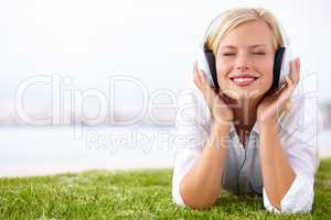 I love this song. Shot of a woman lying on a grassy field listening to music with her eyes closed.